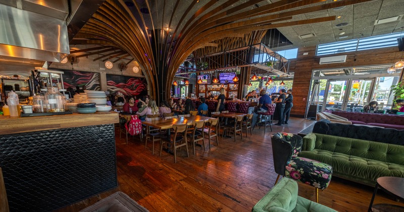 Restaurant interior with wooden furniture, green sofas, and a lively bar area