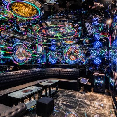 Neon karaoke room with curved seating and colorful ceiling lights.