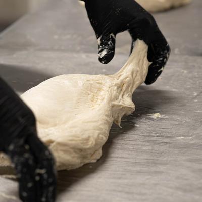 Gloved hands stretching and folding a piece of dough.
