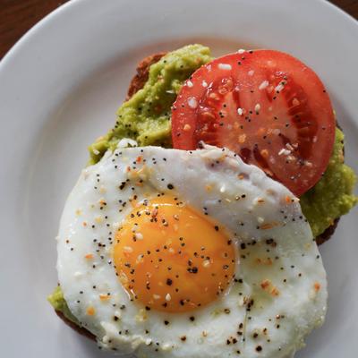 Avocado toast topped with a tomato slice and a fried egg sprinkled with seasoning.