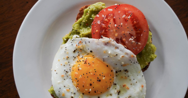 Avocado toast topped with a tomato slice and a fried egg sprinkled with seasoning