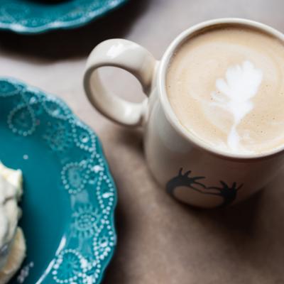 Latte mug sits next to a blue plate with a cinnamon roll.