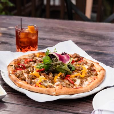 Peppers and Sweet Italian Sausage Pizza served alongside a cocktail.