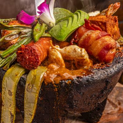 Mixed molcajete with bacon-wrapped shrimp, chorizo, grilled cactus, and avocado.