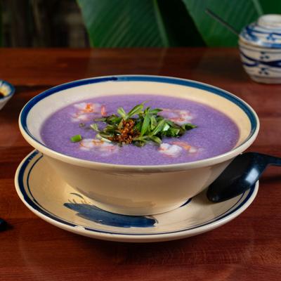 Bowl of creamy purple yam soup with prawns and herb garnish.