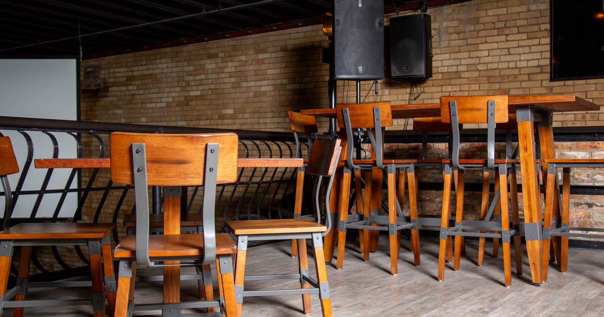 Wooden bar tables and chairs in an interior with exposed brick wall and black ceiling beams
