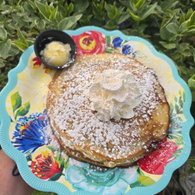 A colorful plate of pancakes topped with whipped cream and powdered sugar, butter on the side.