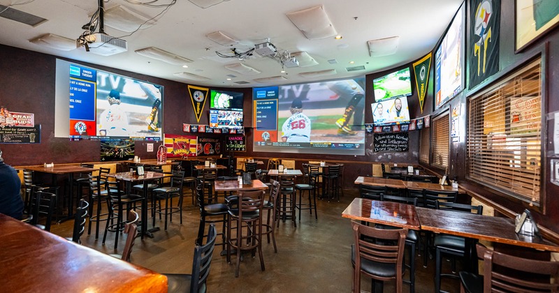 Interior, sports bar section, high seating tables with stools, TVs, projector canvases