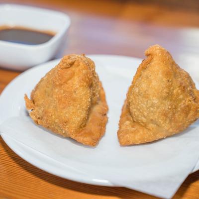 Two samosas and sauce in the background.