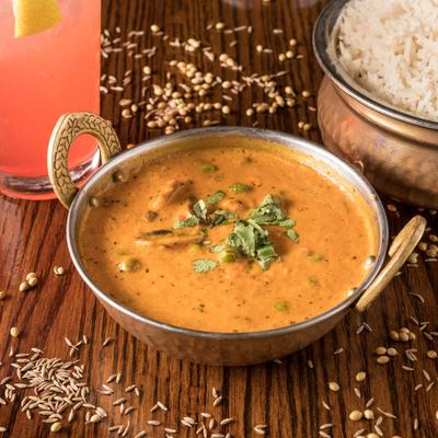 Bowl of mushroom and peas curry with rice and a drink on a table.