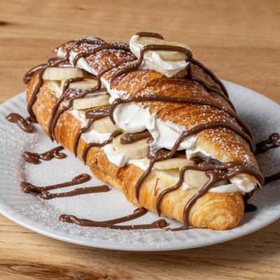 Banana Cream Croissant topped with chocolate drizzle and powdered sugar.