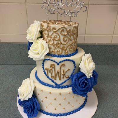 A three-tiered cake garnished with blue and white roses and golden ornaments wedding cakes