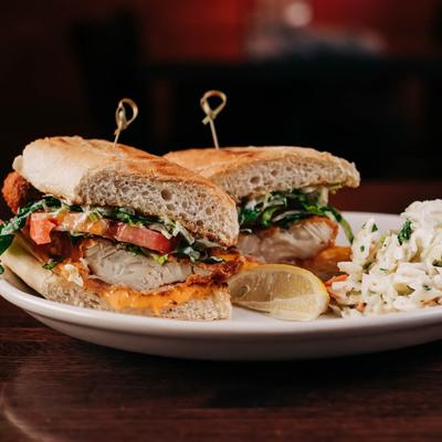 Crispy fried fish sandwich with lettuce, tomato, and coleslaw on the side.