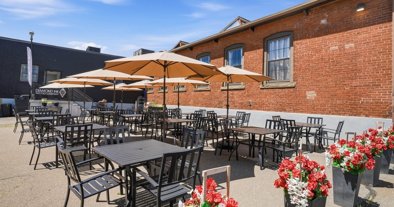 Outdoor patio with black tables and chairs under beige umbrellas