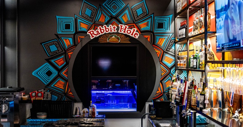 A colorful bar interior Rabbit Hole with a circular mural with geometric designs & the name in red