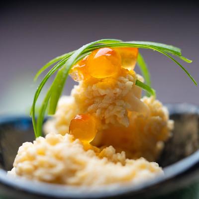 A creamy dish topped with orange fish roe and green herbs, close up.