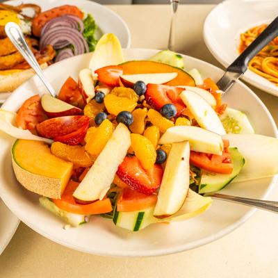 A plate holds fruit salad, surrounded by assorted food plates.