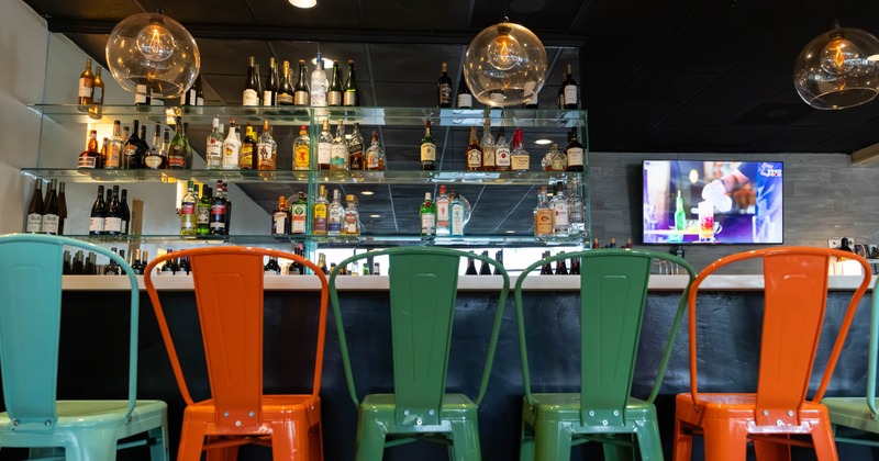Colorful metal chairs in turquoise, orange, and green are lined up at a bar