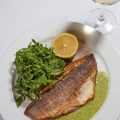 Pan-fried branzino fillet served with pesto, a side of arugula and a lemon half.
