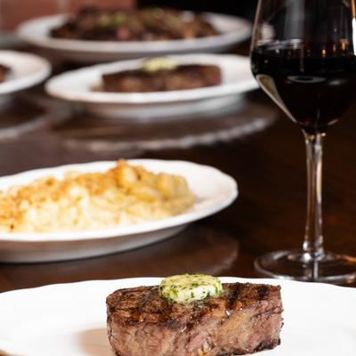 Center cut filet served with glass of wine alongside other dishes.