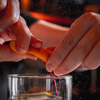 Hands squeezing citrus peel over a cocktail glass.