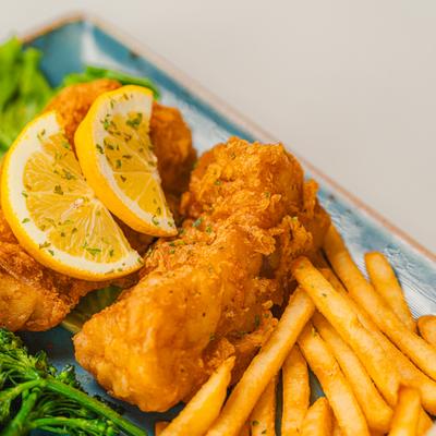 Fried cod with lemon wedges on a blue plate, accompanied by crispy fries and vibrant green broccoli.