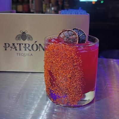 A v red cocktail with a chili powder rim and dried lime slices, set on a metallic table.