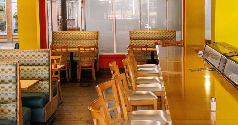 Interior of a restaurant with booth seating and a long countertop lined with chairs.