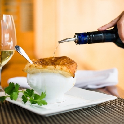 A bottle pours liquid onto a golden pastry-topped soup bowl.