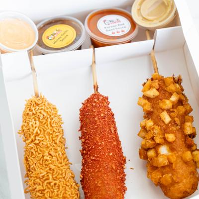 Three crispy Korean corn dogs with unique ramen, spicy, and potato cube coatings.