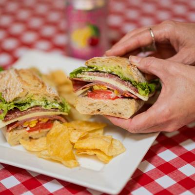 Hands holding a half of Italian club sandwich above the plate with a side of chips.