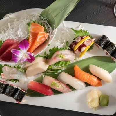 Assorted sushi and sashimi platter, garnished with green leaves and a flower.