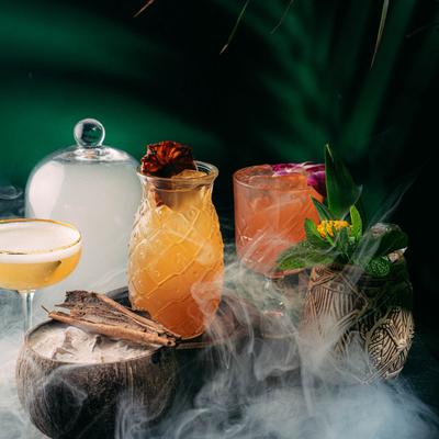Assorted tropical cocktails with smoke rising above against a dark background.