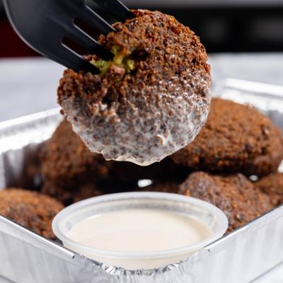 A falafel ball dipped in a creamy white sauce on a tray with more falafel.
