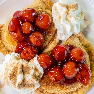 Sweet cheese pierogi, encrusted with graham cracker crumbs, with cherries and whipped cream.
