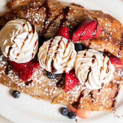 Crepes topped with powdered sugar,  berries, whipped cream, and chocolate drizzle.
