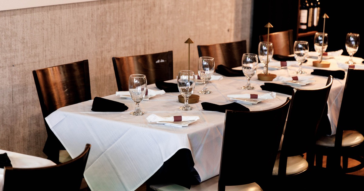 A dining table set with white tablecloth, glasses, and black napkins in a restaurant setting