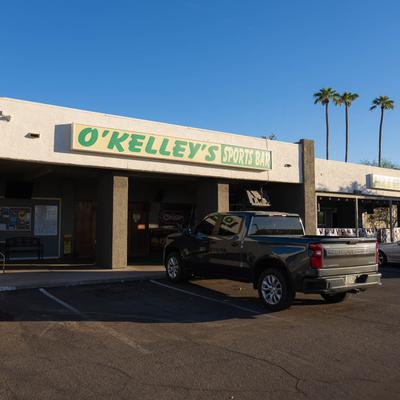 Storefront with signage, palm trees, and a parked car.