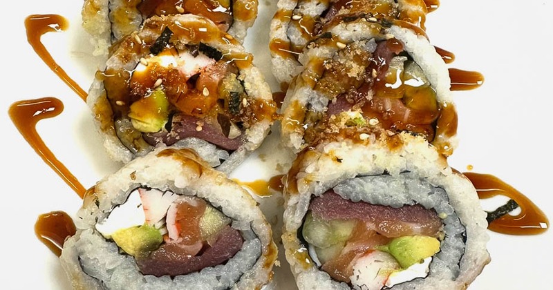 A sushi roll on a white plate, garnished with soy glaze, pink ginger slices, and wasabi