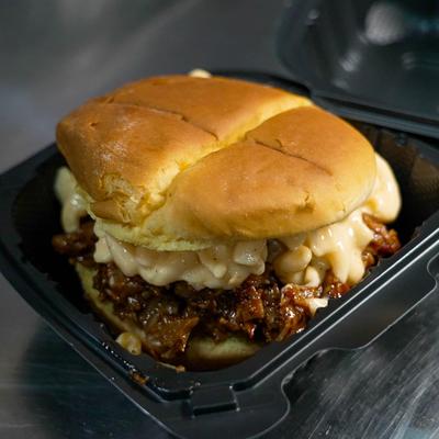 Pulled pork sandwich with mac and cheese in a takeout container.
