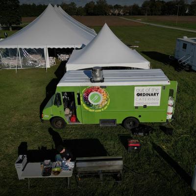A green food truck parked in a grass field with white tents