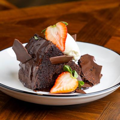 Chocolate cake slice topped with strawberries, cream, and chocolate shards.