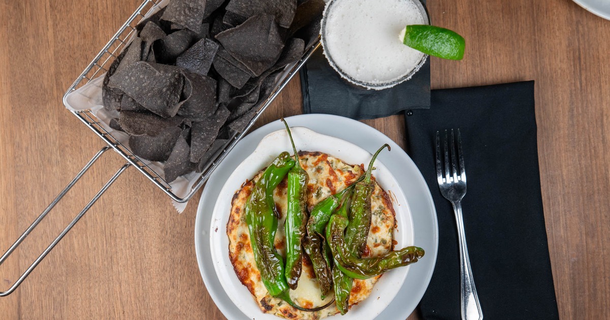 Top view of shishito peppers with blue corn chips and a beer
