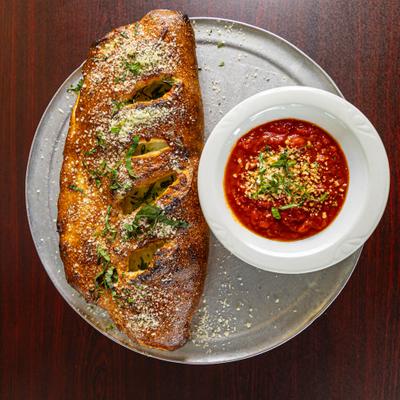 Overhead view of a baked calzone served with marinara sauce.