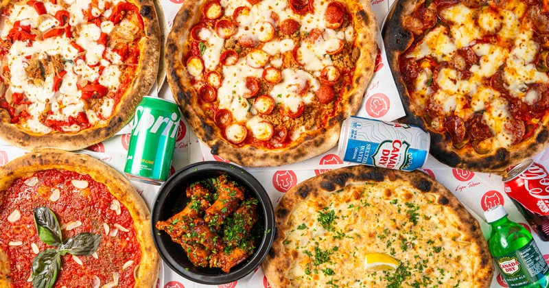 Assorted pizzas, sodas, and chicken wings on a table
