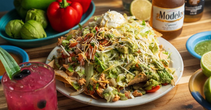 Plate of loaded nachos served on the table with a cocktail and a bottle of beer