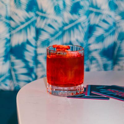A red cocktail on a white table, the background is a blue and white tropical leaf pattern.