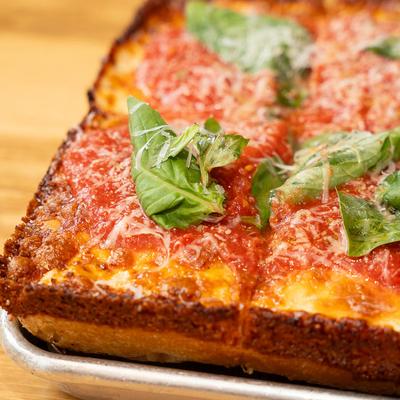 Close-up of a square pizza with tomato sauce, cheese, and basil.