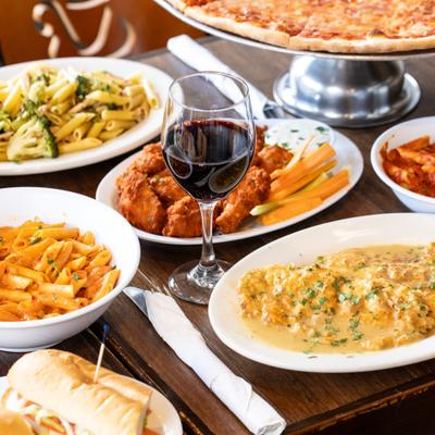 Assorted pasta dishes, chicken wings, pizza, and red wine on a table.