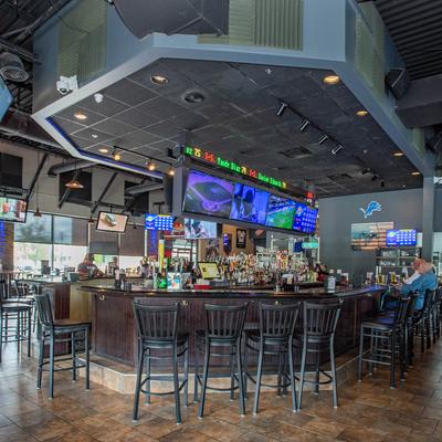 Interior featuring wooden bar top with numerous dark bar stools arranged in front of it.